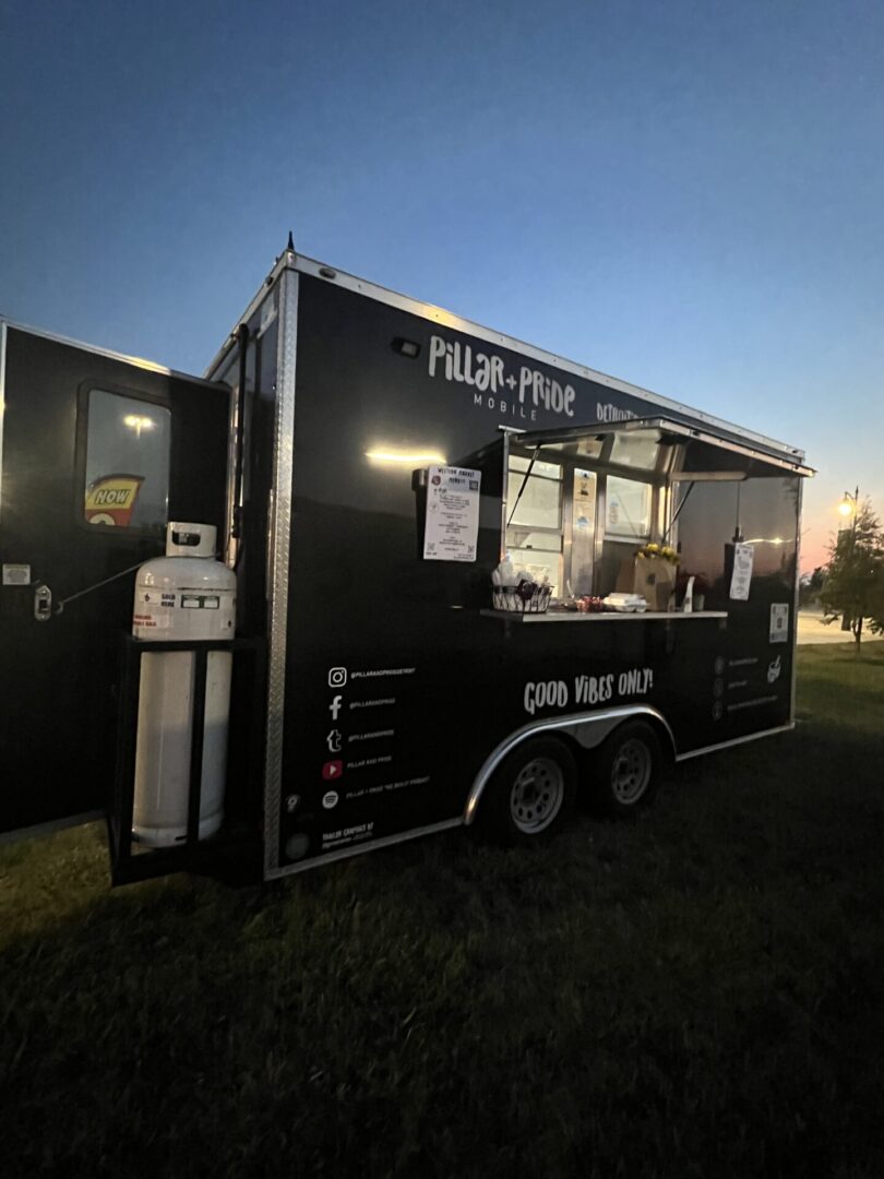 A black food truck parked in the grass.